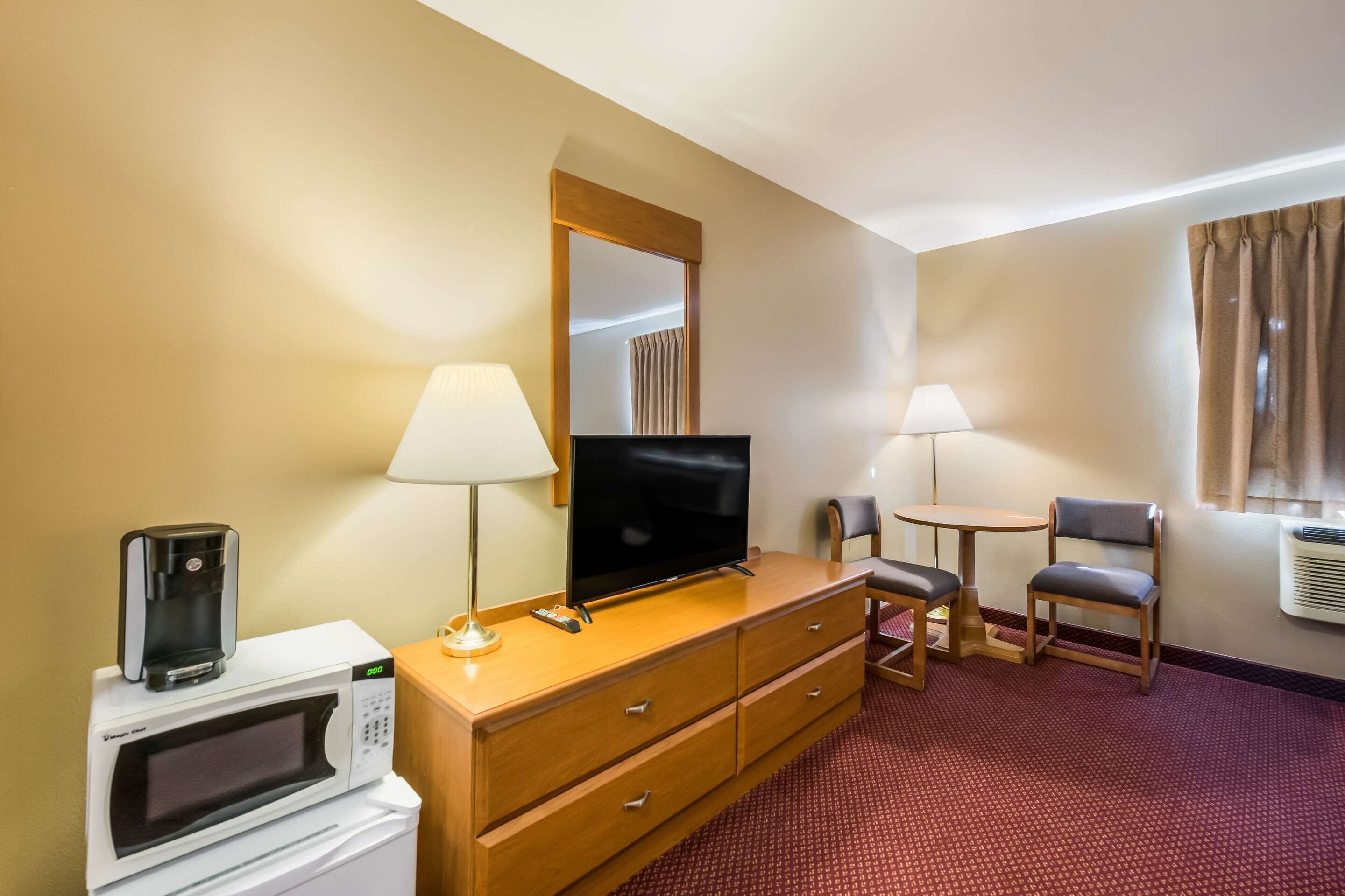Et hotelværelse med mikrobølgeovn, fjernsyn, skrivebord med lampe, stol og et vindue med gardiner.