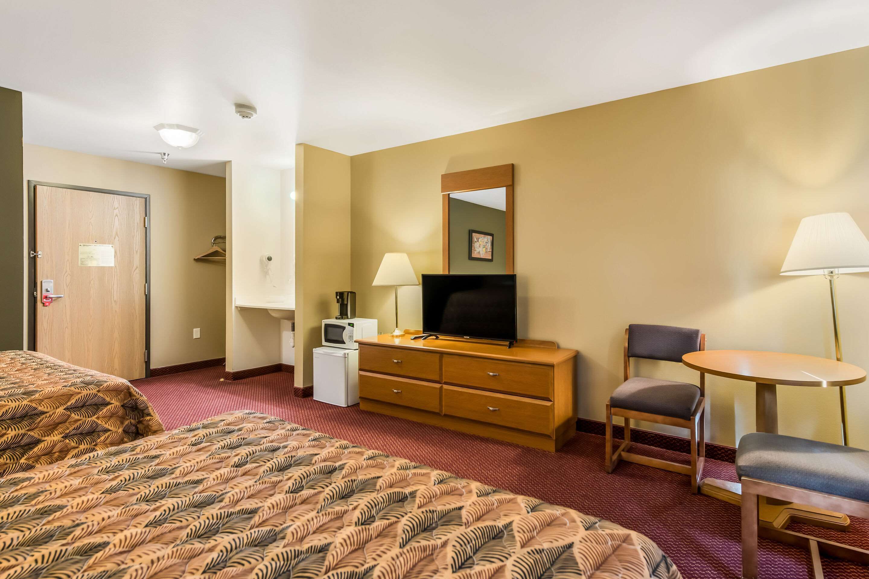 A hotel room with a bed, a desk, a chair, a TV, a lamp, and a small refrigerator.