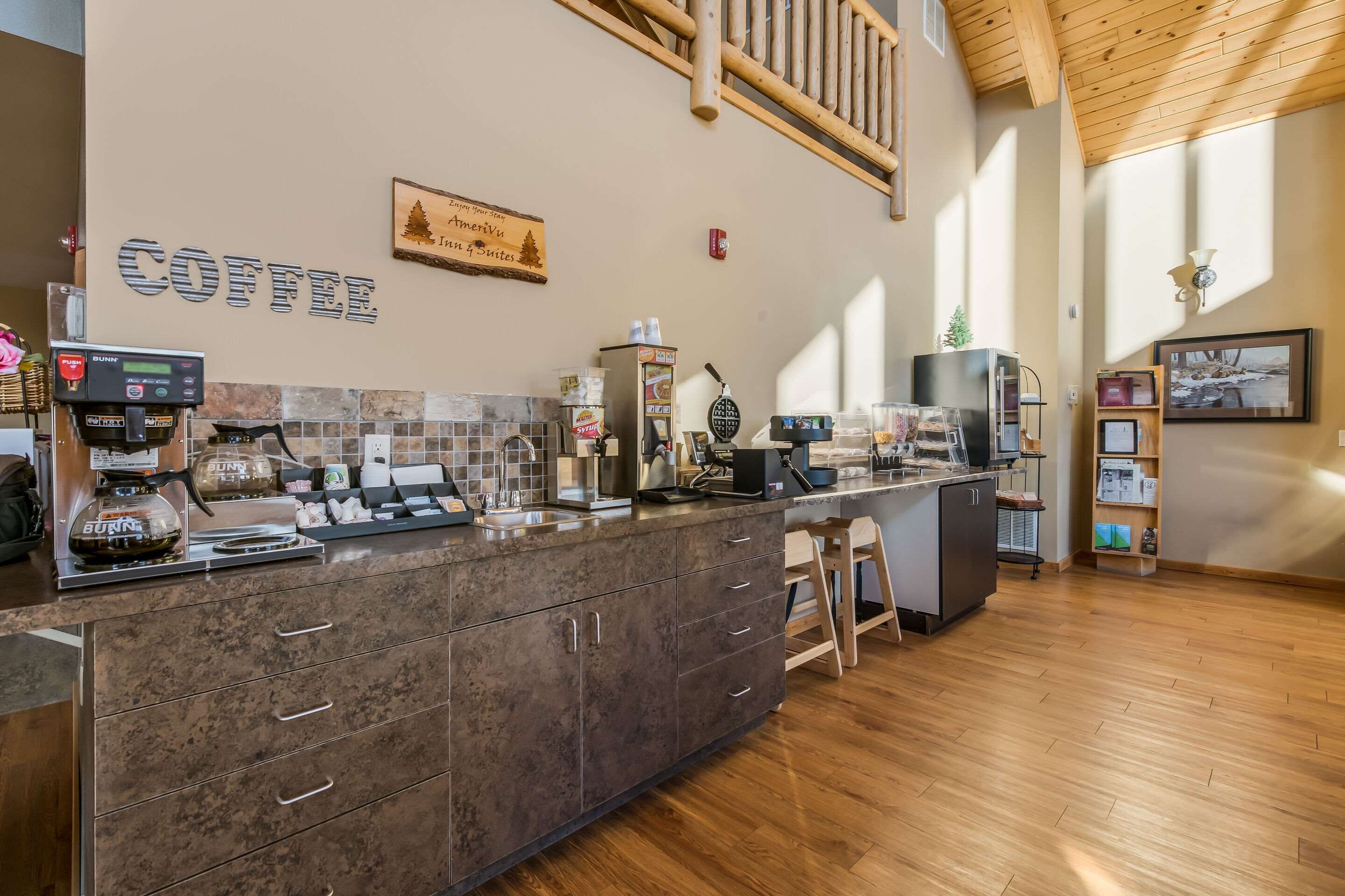 A modern coffee bar with a stone countertop, coffee machines, and a wooden ceiling.