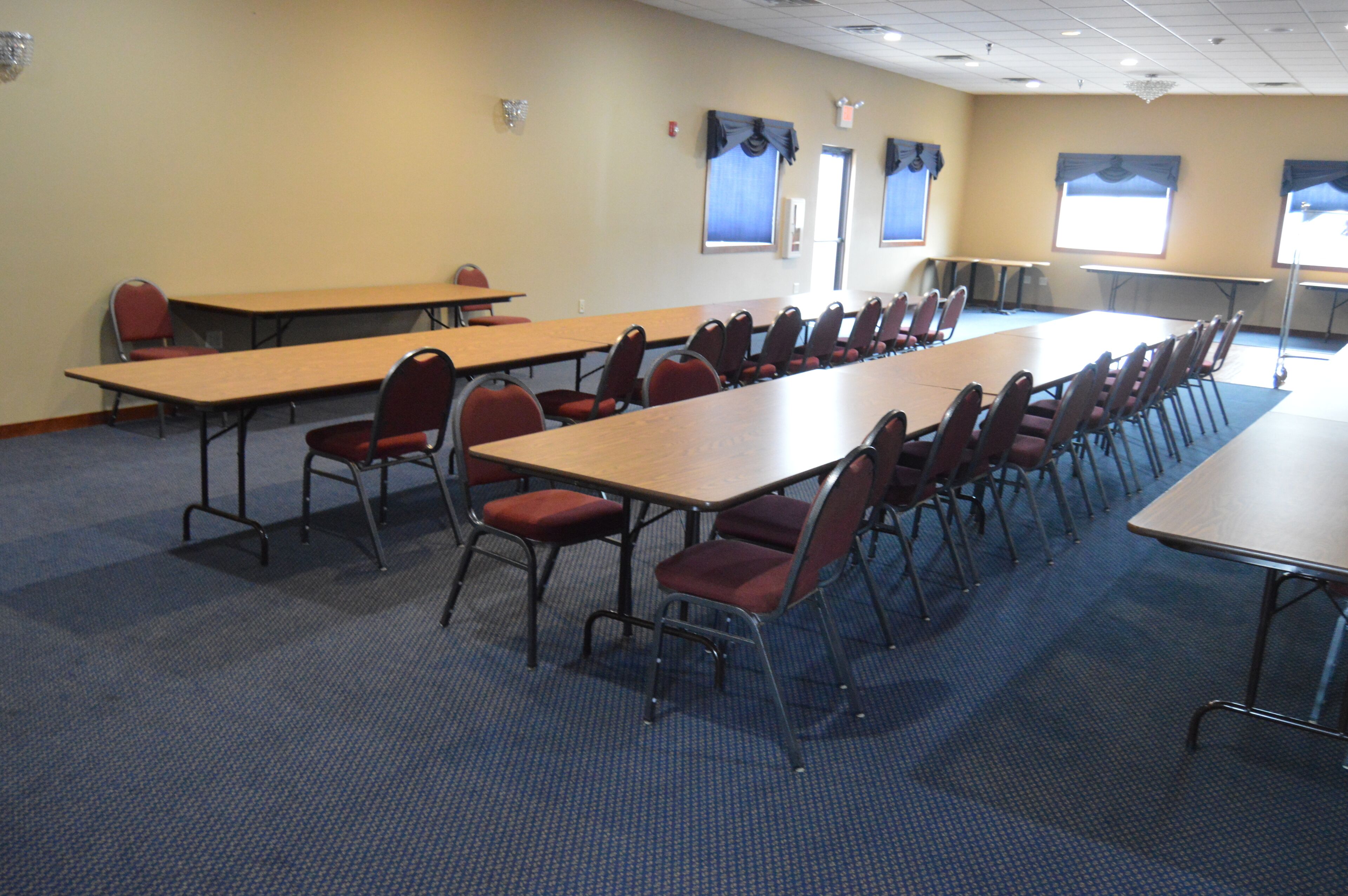 A conference room with long tables and chairs, carpeted floor, and windows with curtains.