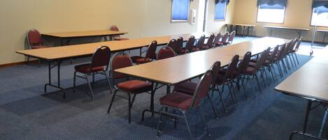 A conference room with long tables and chairs, carpeted floor, and windows with curtains.