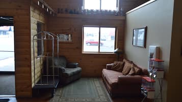 Una habitación acogedora con paredes de madera, un sillón de cuero, un sofá marrón, una estantería metálica y una ventana que ofrece vistas a un coche rojo.