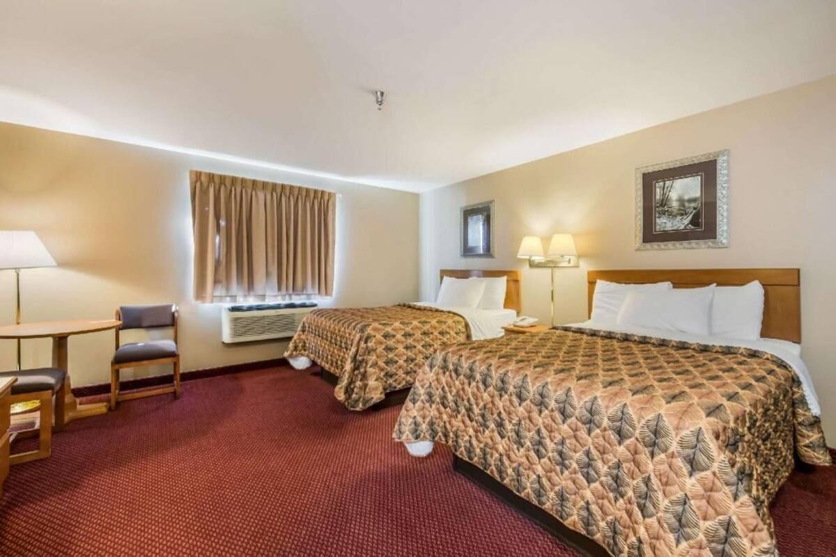 A hotel room with two beds, a desk with a chair, a window with curtains, and a wall-mounted picture.