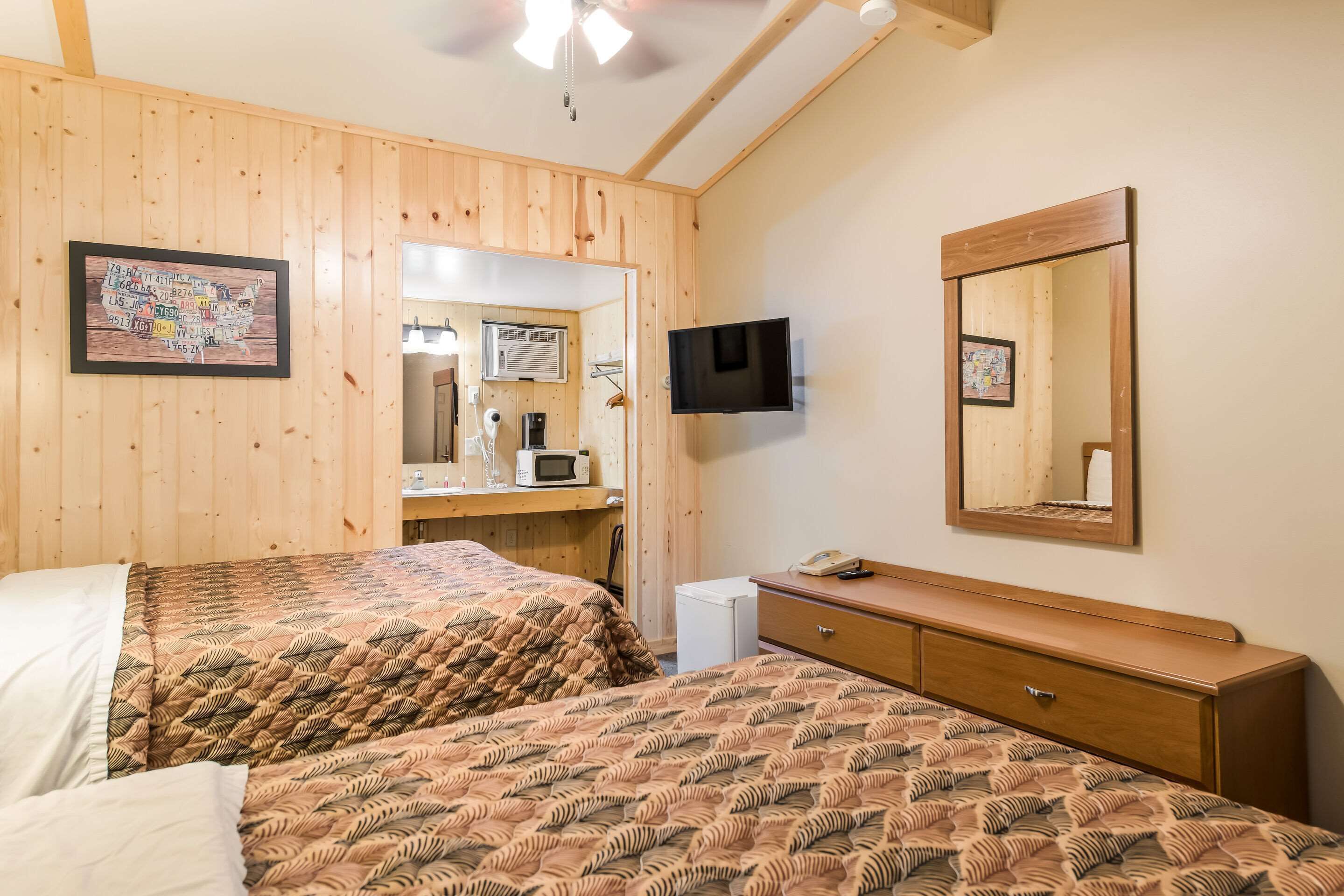 A room with two beds, a wooden dresser, a television, and a mirror.