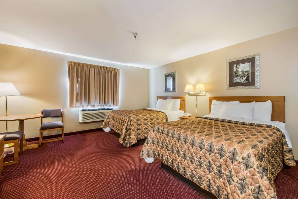 A hotel room with two beds, a desk, a chair, and a window with curtains.
