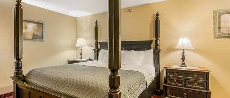 A four-poster bed with a wooden frame, a nightstand with a lamp, and a dresser with drawers.
