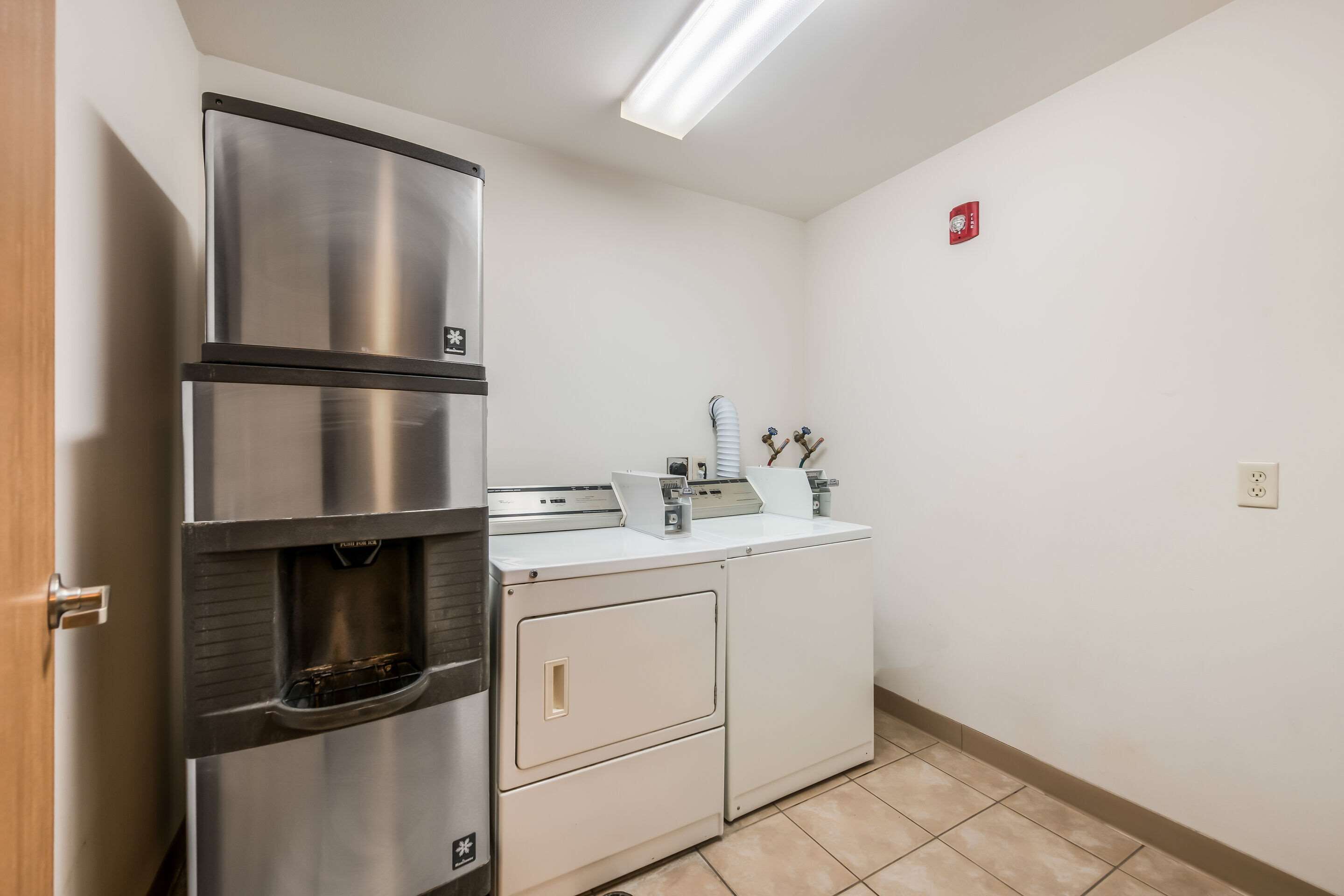A compact kitchen with a stainless steel refrigerator, a built-in washing machine, and a small countertop with a coffee maker.