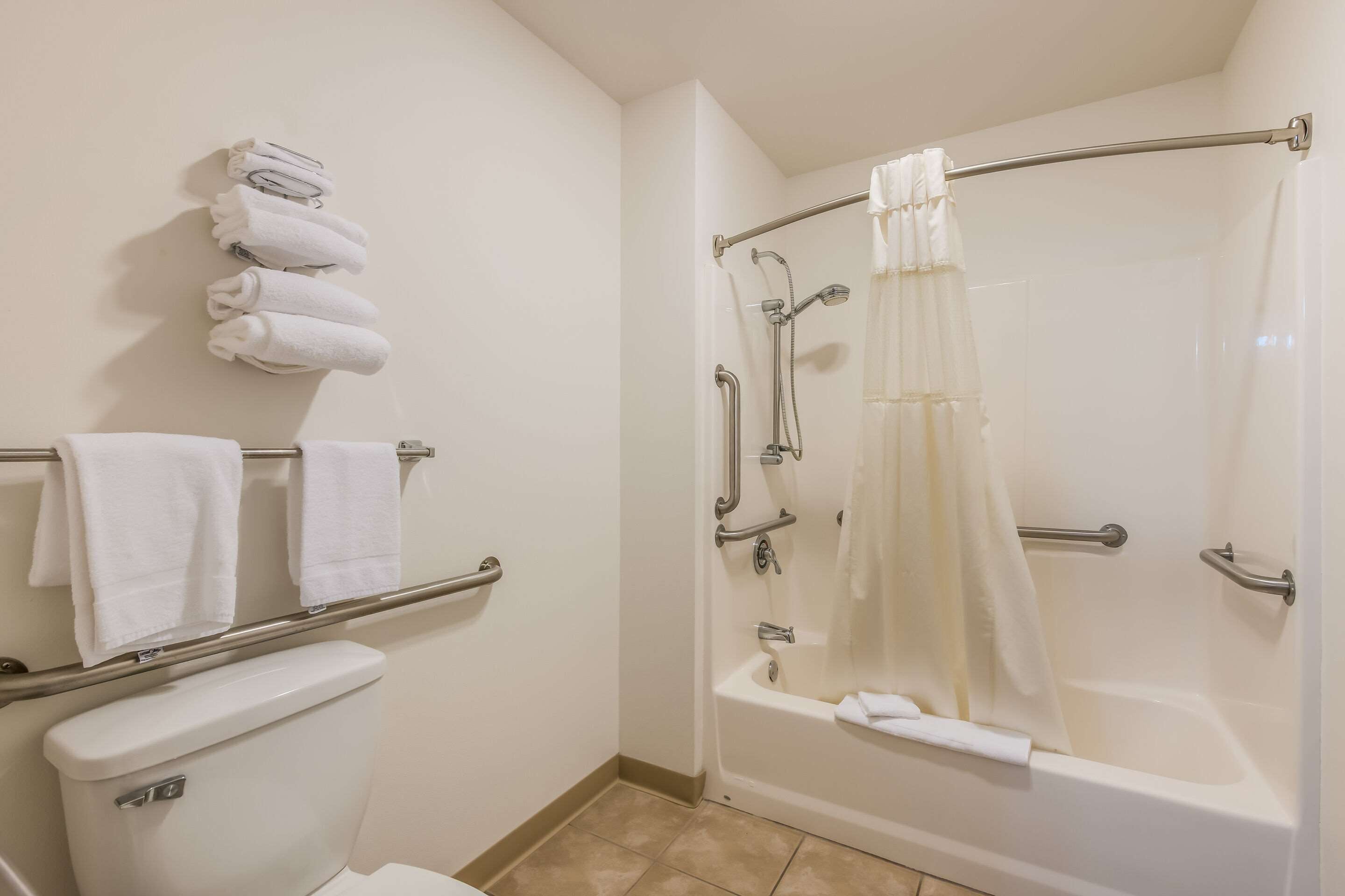 A bathroom with a toilet, a bathtub with a shower curtain, and a towel rack with several towels.