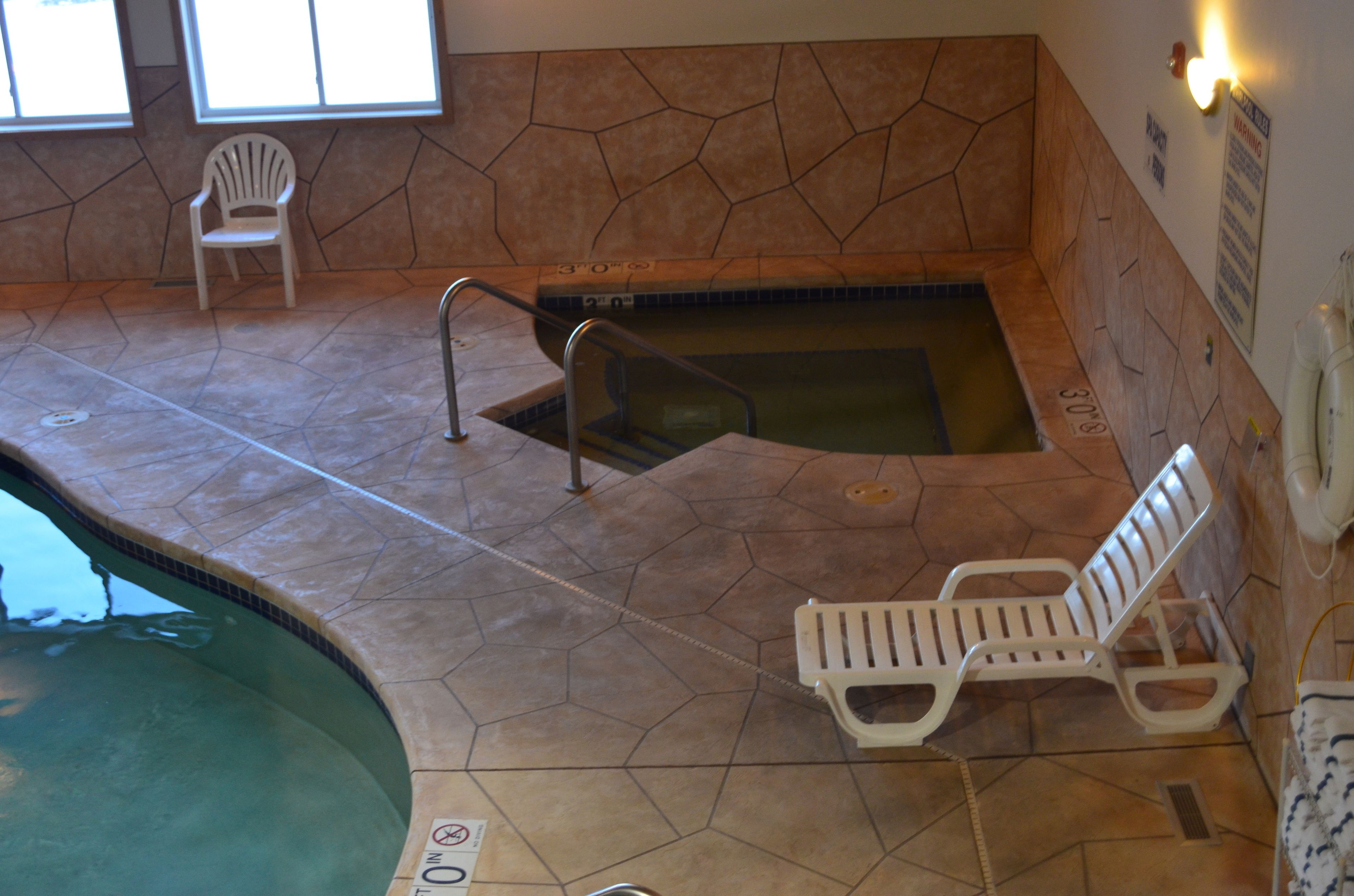 A swimming pool area with a stone wall, two white lounge chairs, and a chair.