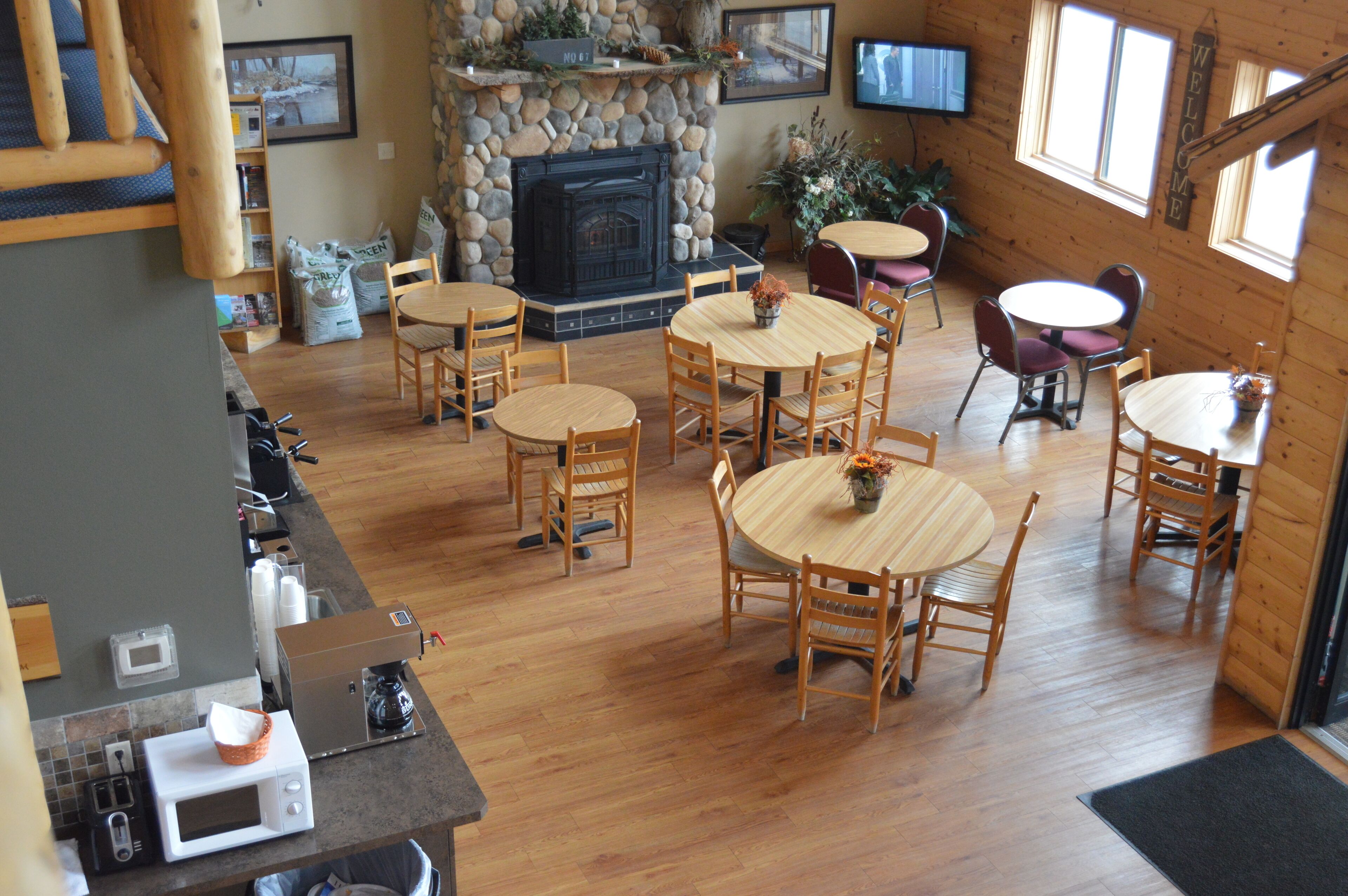 A cozy cabin-style interior with a stone fireplace, wooden dining tables, and a television mounted on the wall.