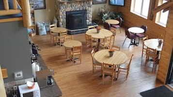 Un interior acogedor estilo cabaña, con una chimenea de piedra, mesas de comedor de madera y un televisor montado en la pared.