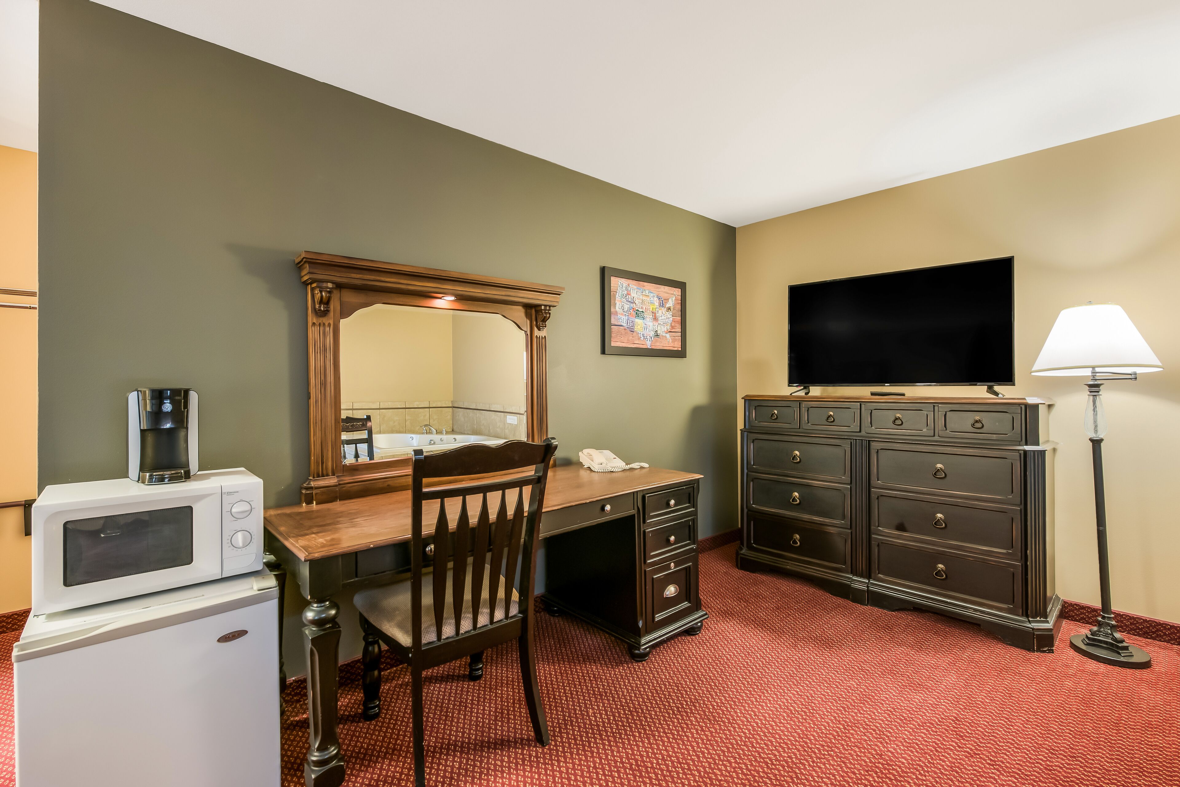 Une chambre d’hôtel équipée d’un bureau en bois, d’une commode, d’une télévision, d’une lampe, d’un four à micro-ondes et d’un réfrigérateur.
