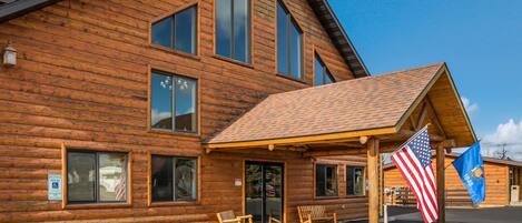 A wooden lodge with a covered entrance, American and state flags, and a parking area with marked spaces.
