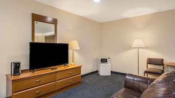 Une chambre d’hôtel équipée d’un téléviseur à écran plat, d’une commode en bois, de deux lampes, d’un four à micro-ondes, d’un canapé en cuir marron et d’une petite table.