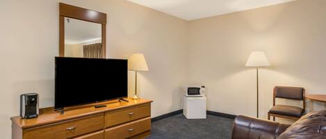 Ein Hotelzimmer mit Flachbildfernseher, Holzkommode, zwei Lampen, einer Mikrowelle, einem braunen Ledersofa und einem kleinen Tisch.