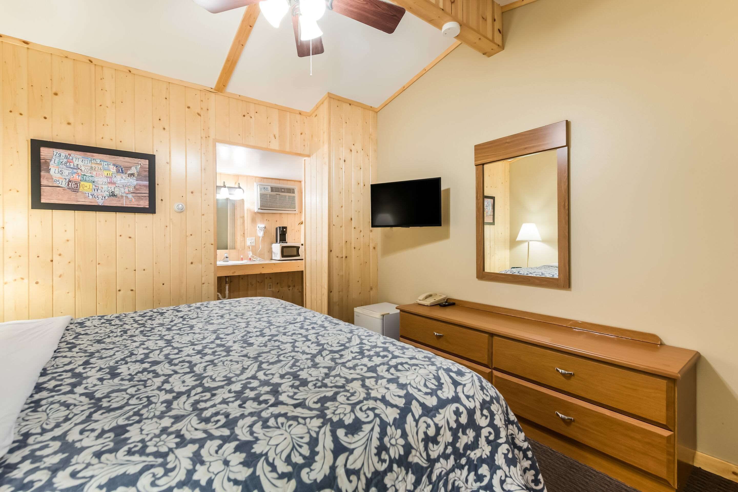 Een hotelkamer met een bed, houten wanden, een televisie, een spiegel, een dressoir en een klein bureau met een lamp.