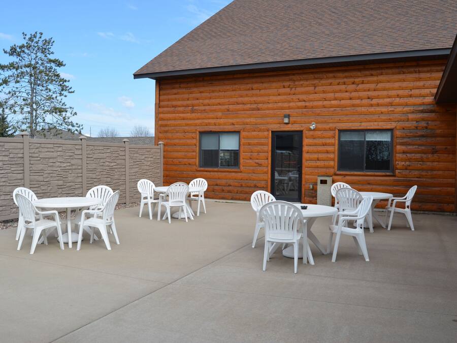 Eine Blockhütte mit einer Terrasse, ausgestattet mit weißen Plastikstühlen und -tischen.