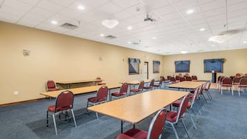 A conference room with multiple tables and chairs, a projector, and a chandelier.