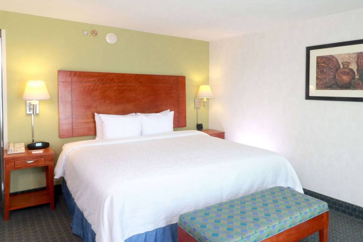 Ein Hotelzimmer mit Bett, Nachttischen, einer Bank und einem an der Wand hängenden Gemälde.