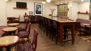 Een restaurant met ronde tafels en stoelen, een lange toonbank en een televisie aan de muur.
