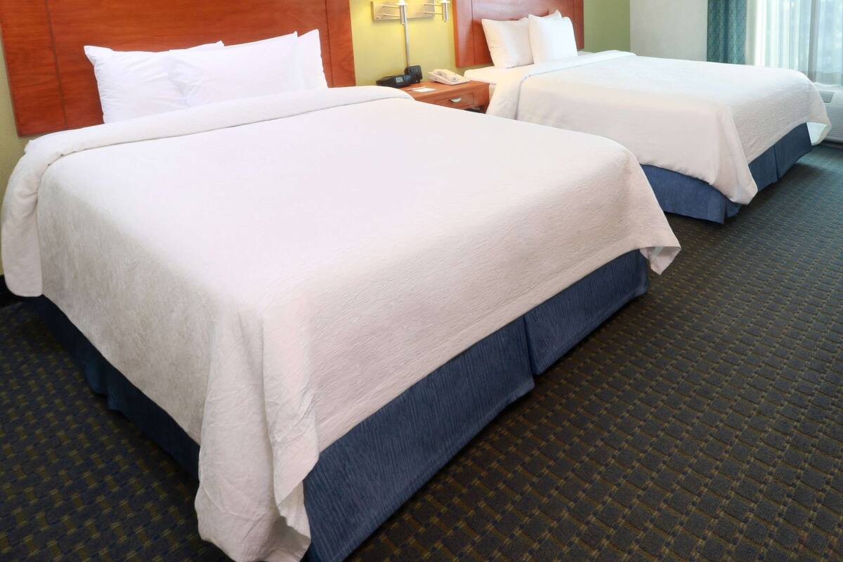 Ein Hotelzimmer mit zwei Betten, einem Holzkopfende, einem Nachttisch mit Lampe und einem gemusterten Teppich.