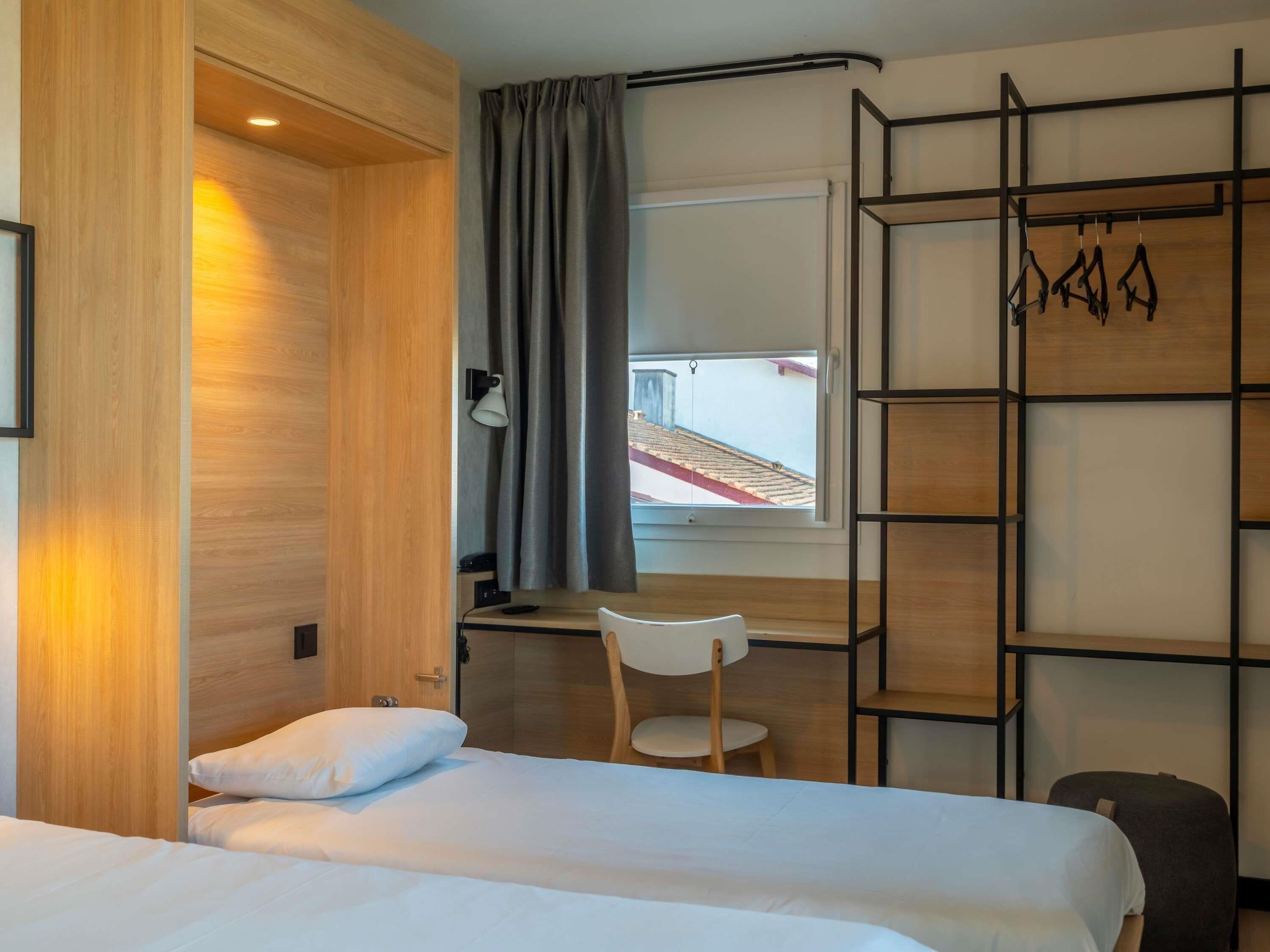 Habitación de hotel con cama, escritorio, silla, armario y ventana con vistas.