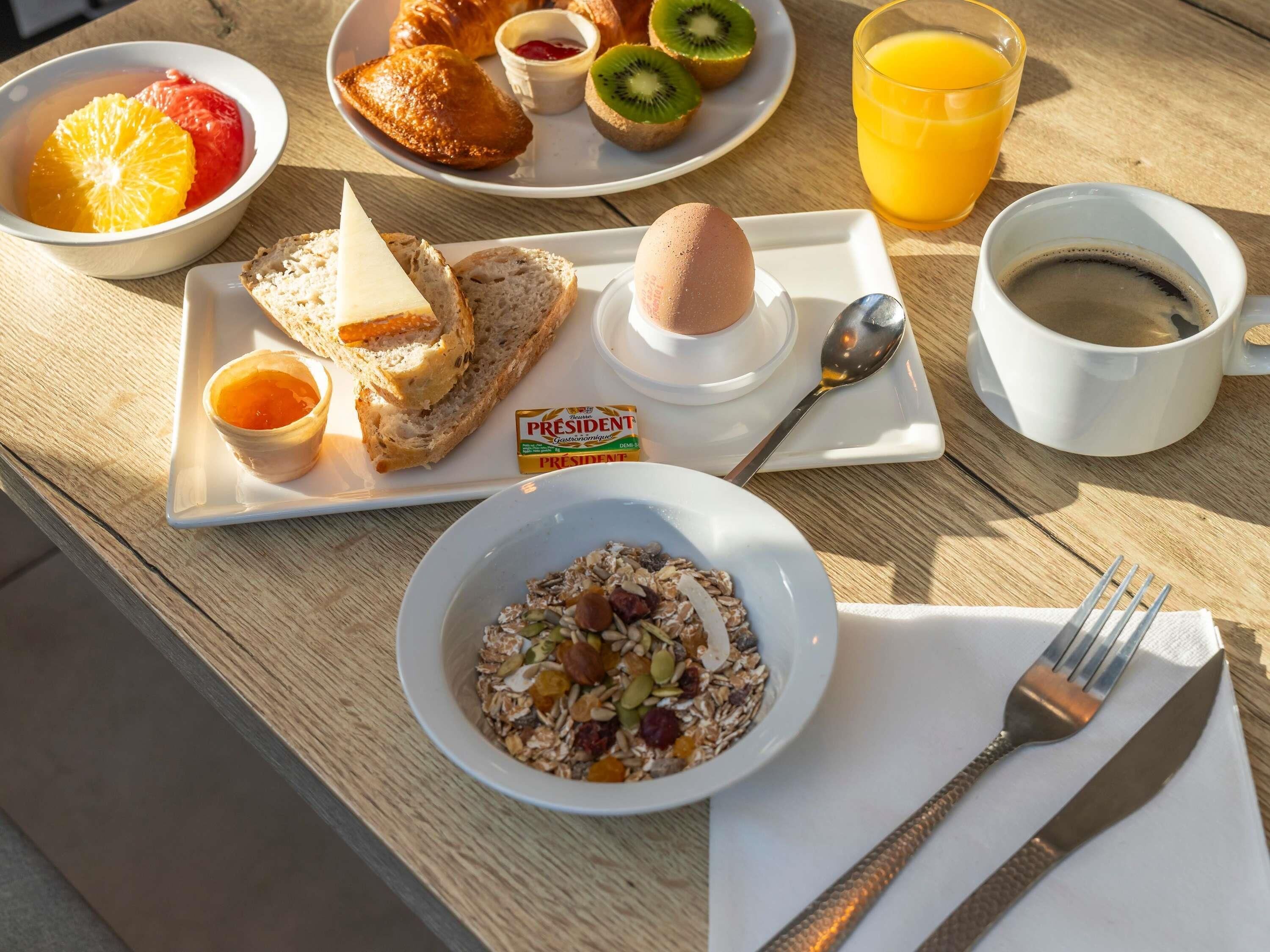 Ein Frühstückstisch mit Croissants, Obst, einer Schüssel Müsli, einer Tasse Kaffee und einem Glas Orangensaft.