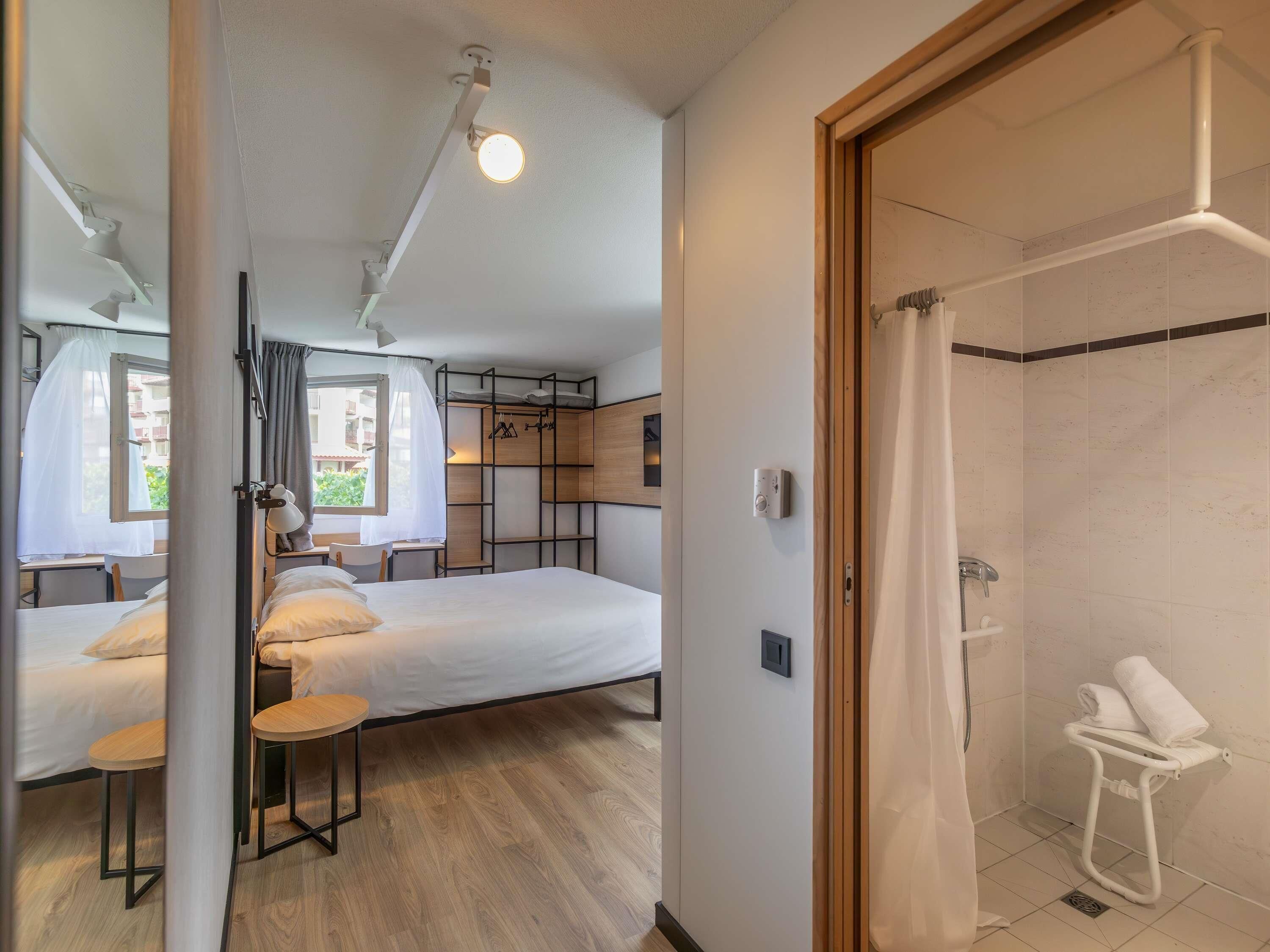 A modern hotel room with a bed, a desk, and a shower area.