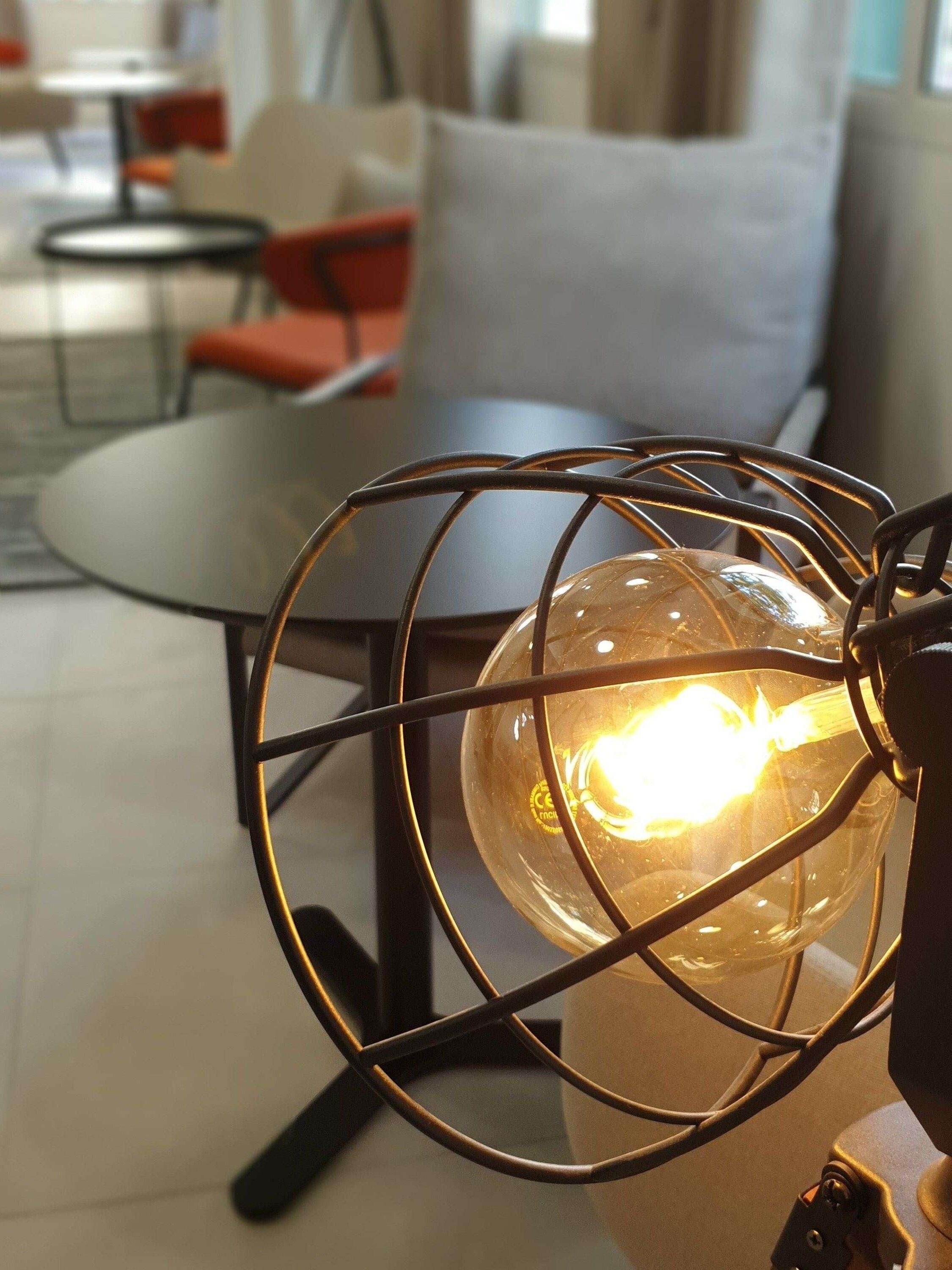 A modern interior with a spherical light fixture encased in a metal frame, a round table, and a sofa with a cushion.