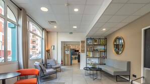 A modern waiting area with seating, a bookshelf, and a view of the outside. - ibis Ciboure St Jean De Luz Hotel (Ciboure)