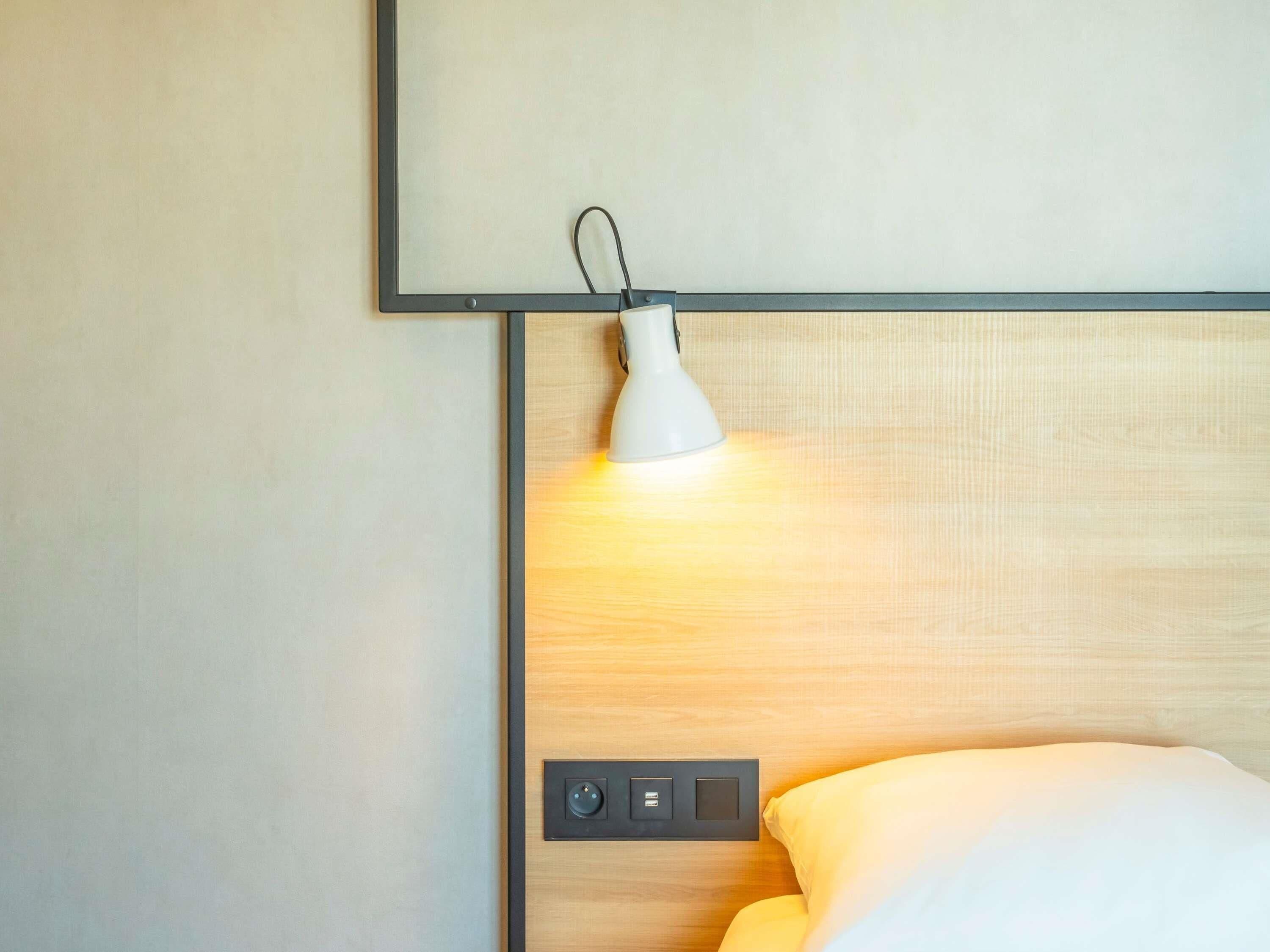 A neatly made bed with a white pillow and a headboard with a light fixture above it.