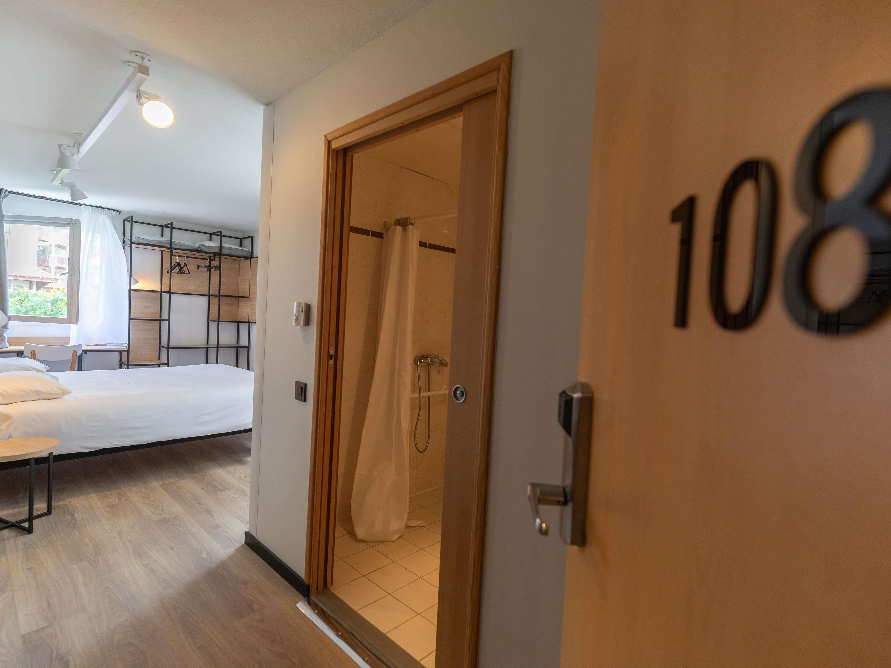 A hotel room with a bed, a shower area, and a door marked with the number 108.