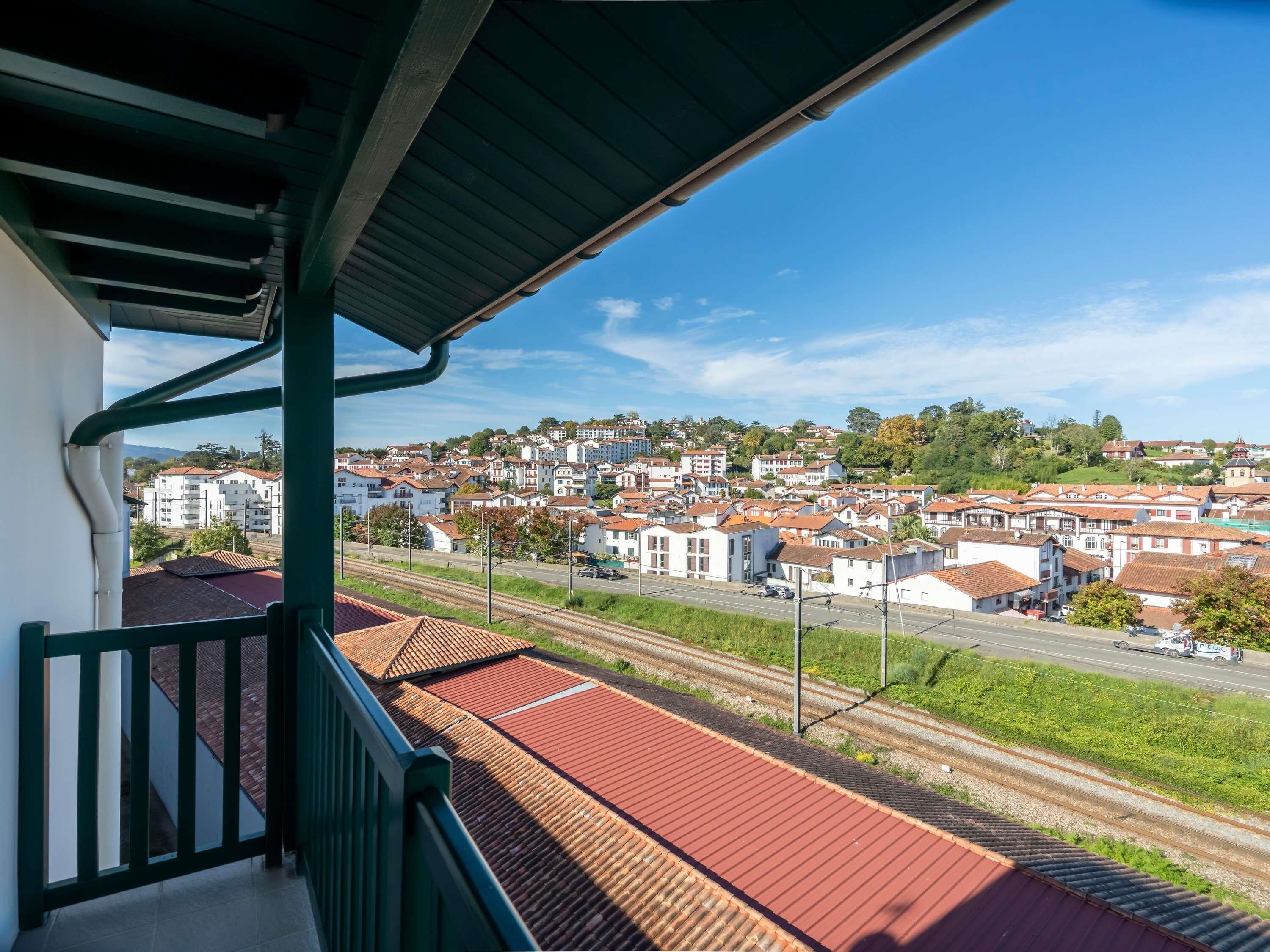 A balcony with a view of a town, railway tracks, and a police car on the road.