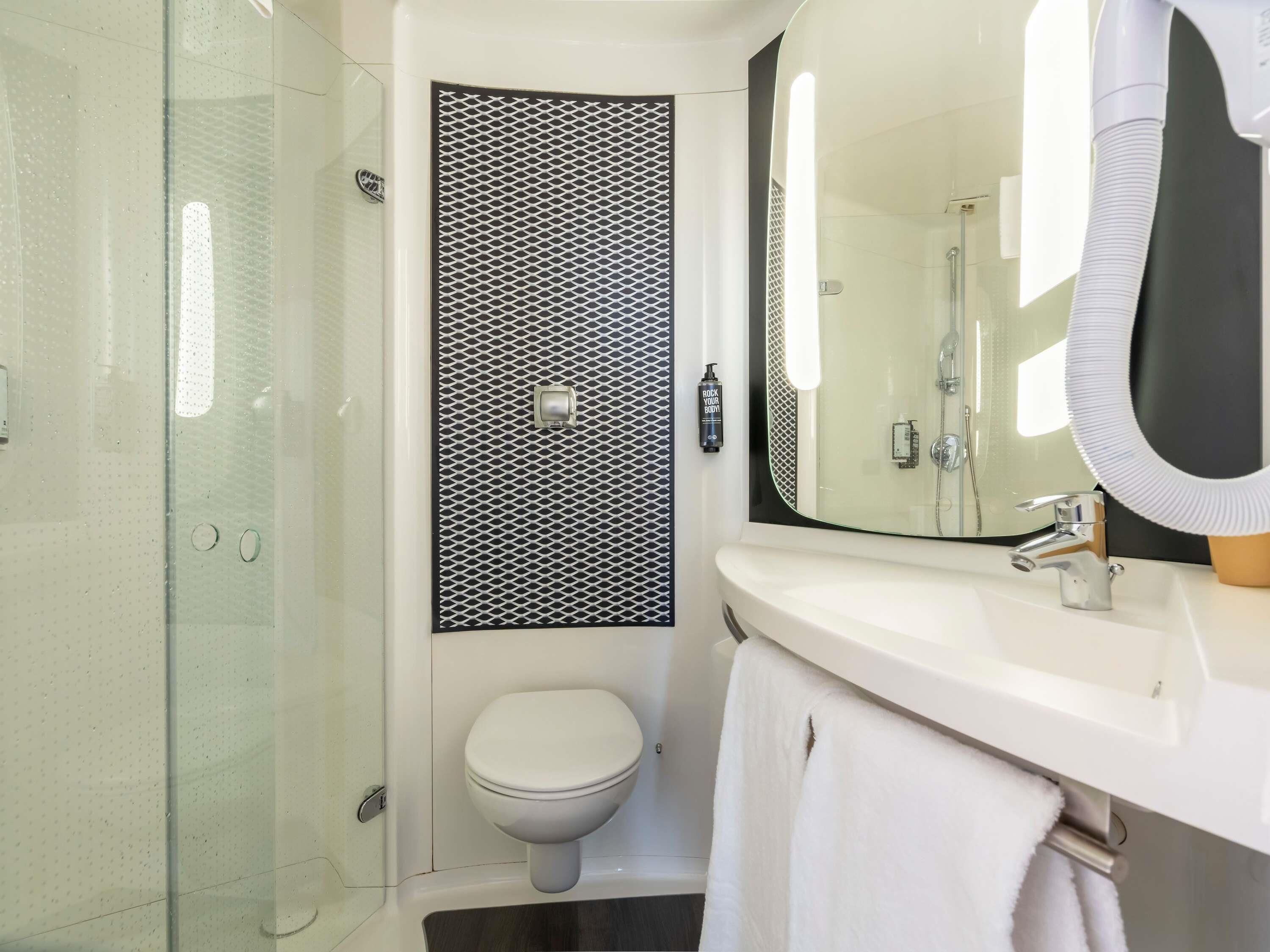A modern bathroom with a glass shower enclosure, a toilet, a sink with a mirror, and a towel rack.