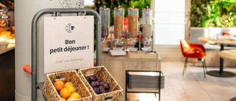 A breakfast setup with baskets of fruits, a sign with French text, and a modern interior with a green wall and seating area.