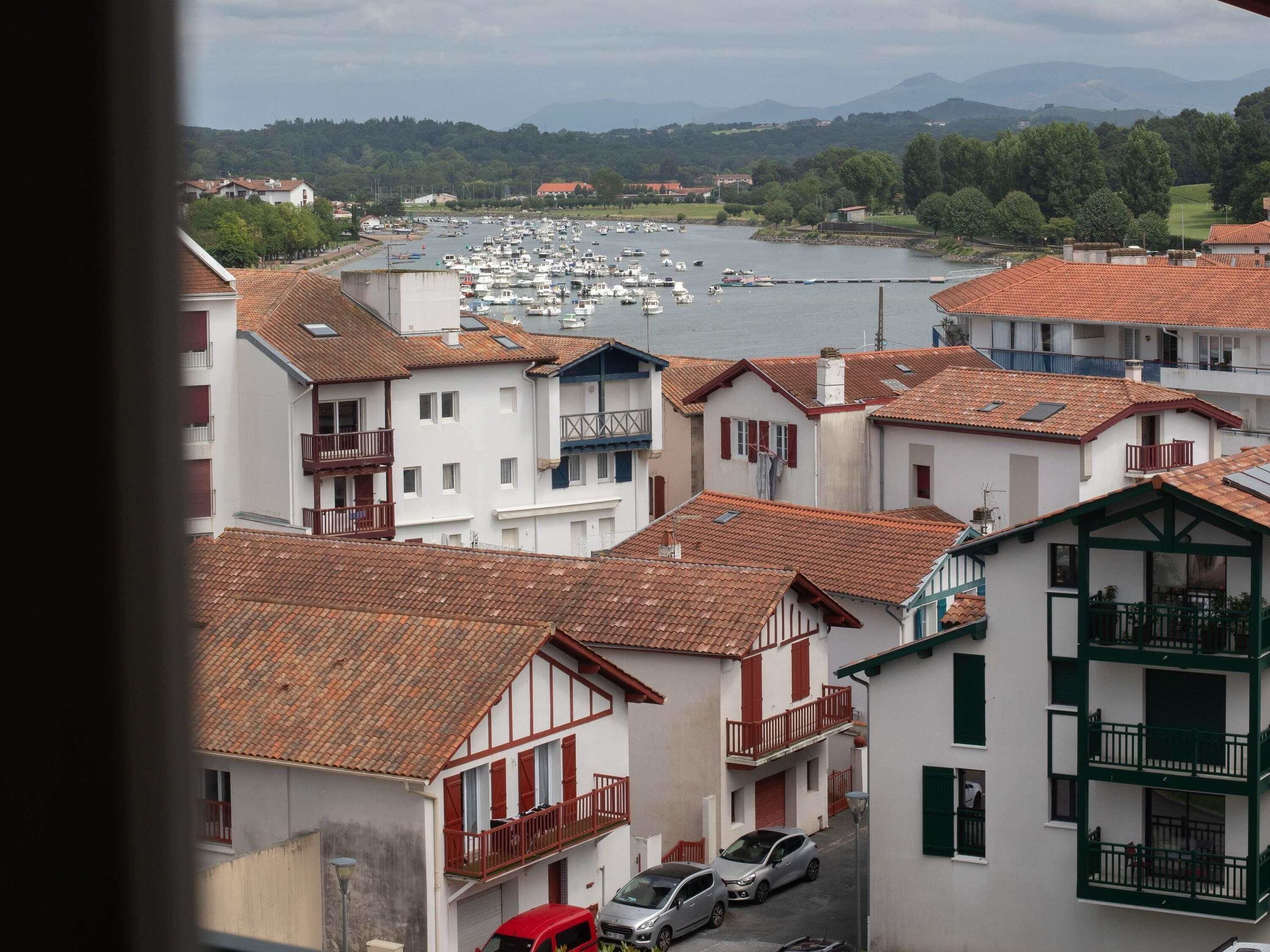 A coastal town with traditional buildings, a marina with boats, and a view of the sea and mountains.