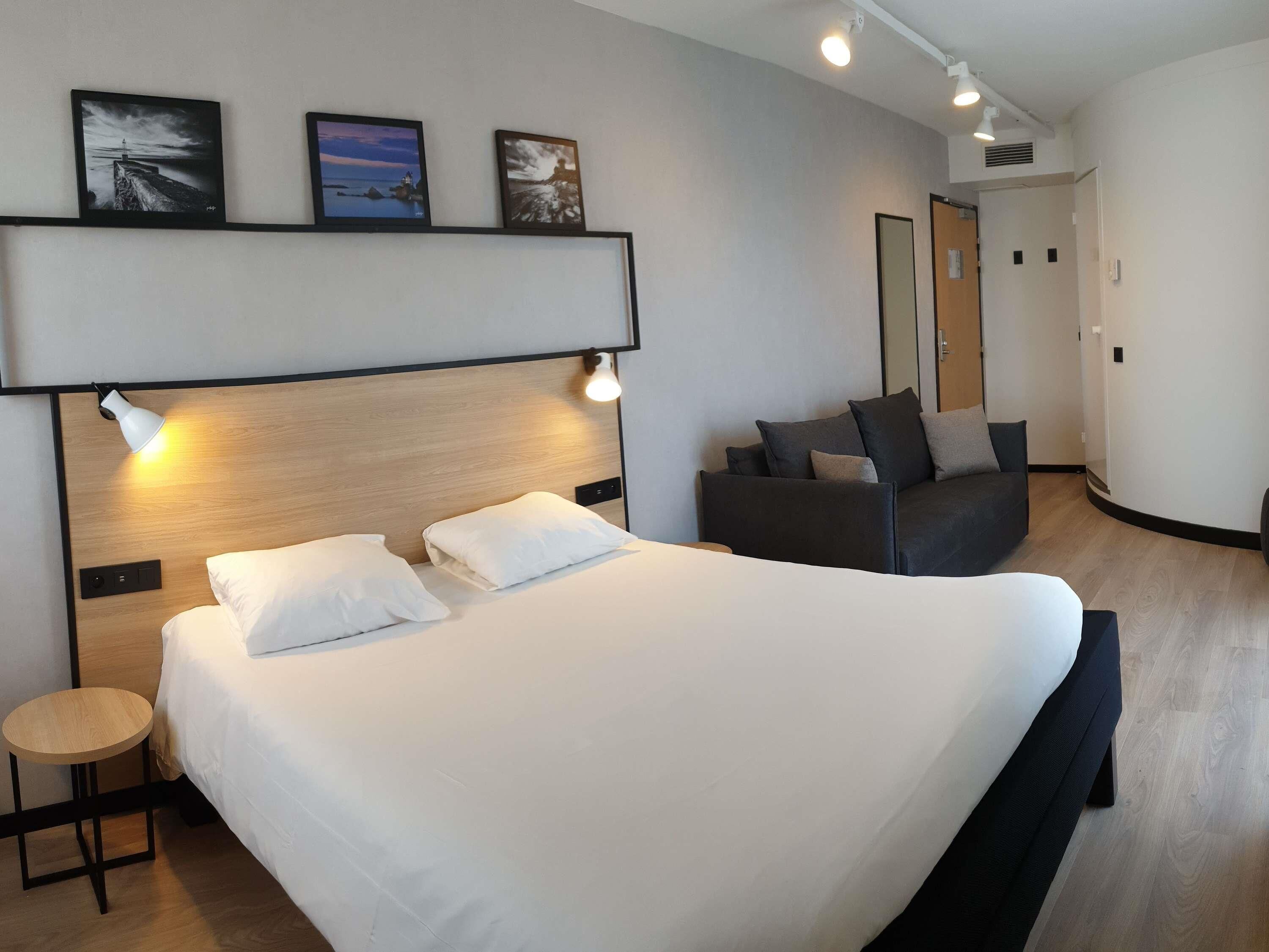 Una habitación de hotel moderna con una cama grande, una pequeña mesa redonda, un sofá y tres cuadros en la pared.