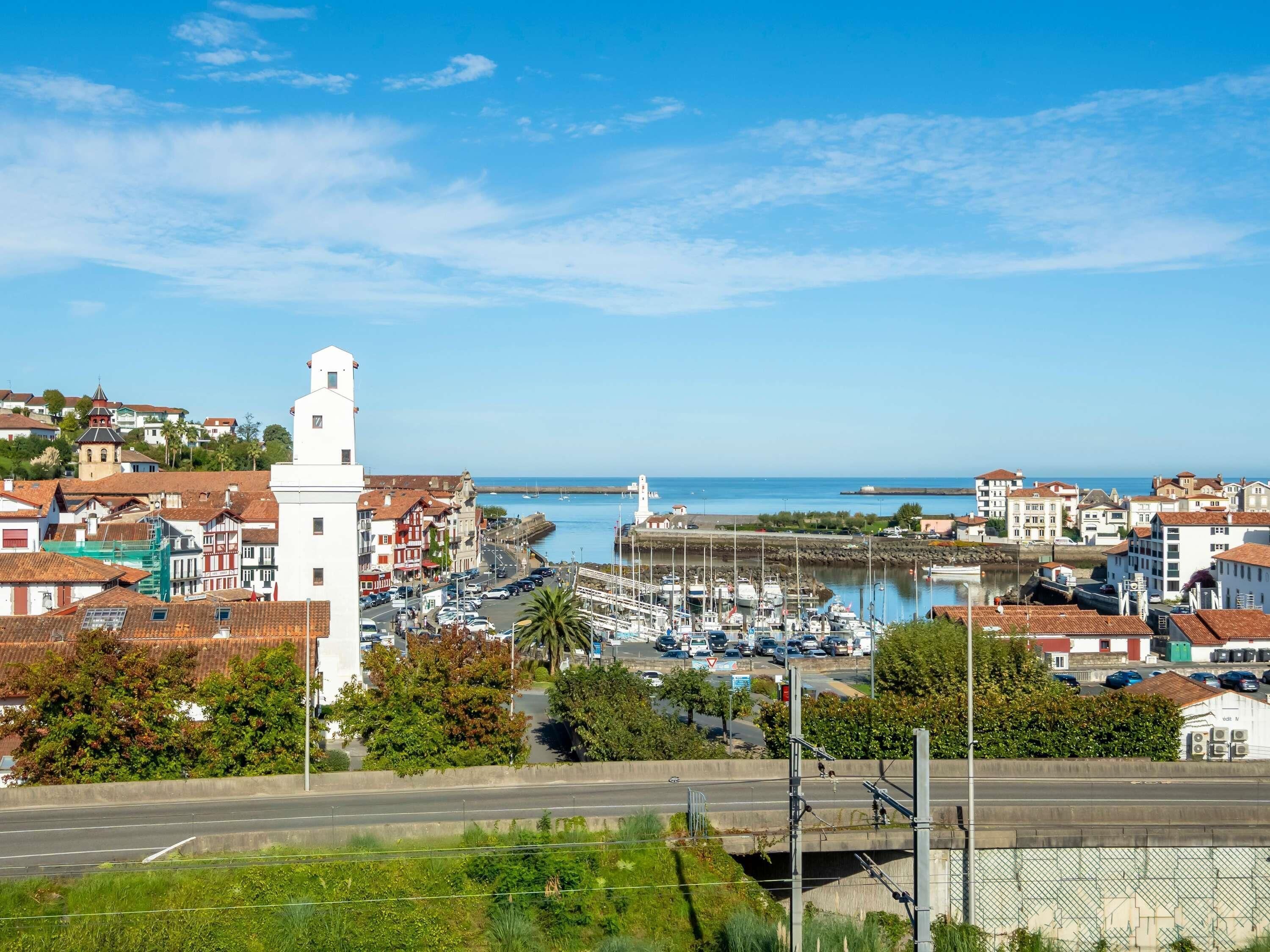 A coastal town with a prominent white tower, a marina with boats, and a mix of residential and commercial buildings.