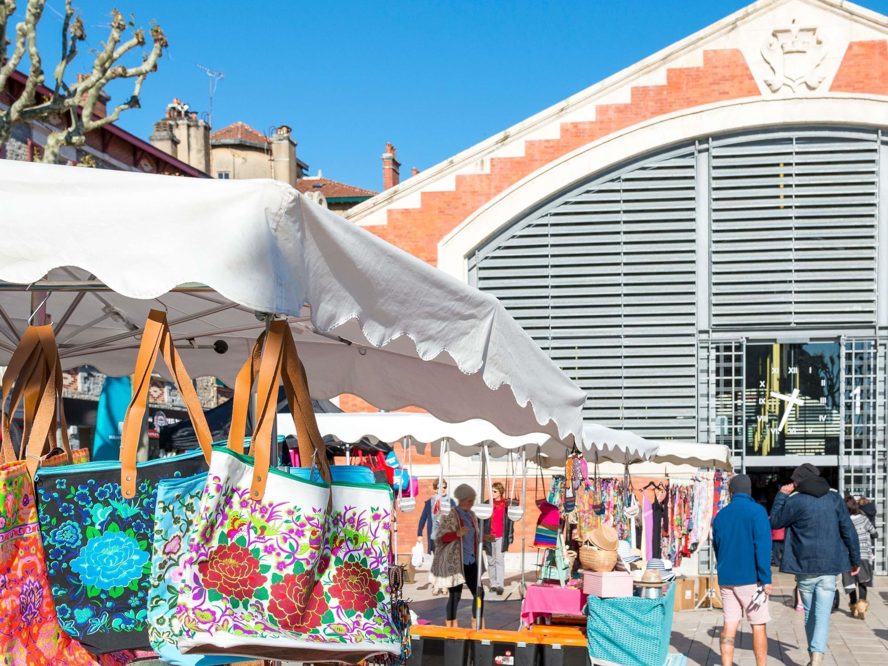 A market stall with colorful bags and a building with a large arched window in the background.