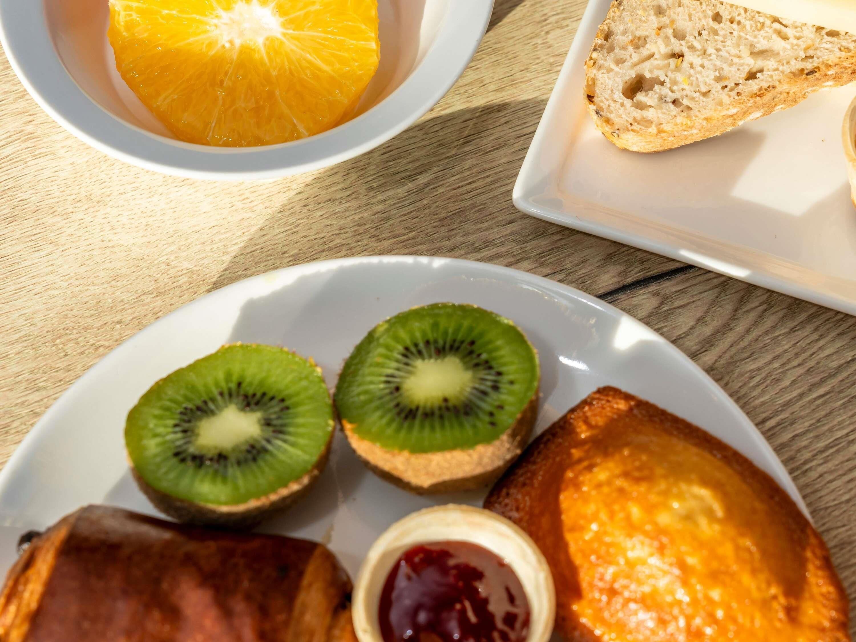 A plate with kiwi slices, toast, jam, and an orange.