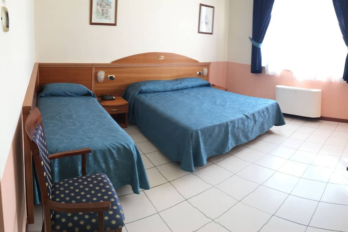 A hotel room with two single beds, a wooden nightstand, a desk with a lamp, and a chair.