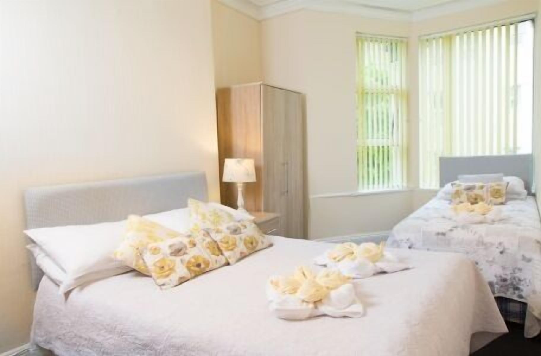 A hotel room with two beds, each with floral bedding and towels. There is a wardrobe and a window with blinds.