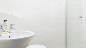 Et badeværelse med en hvid vask, toilet og en brusekabine i glas.