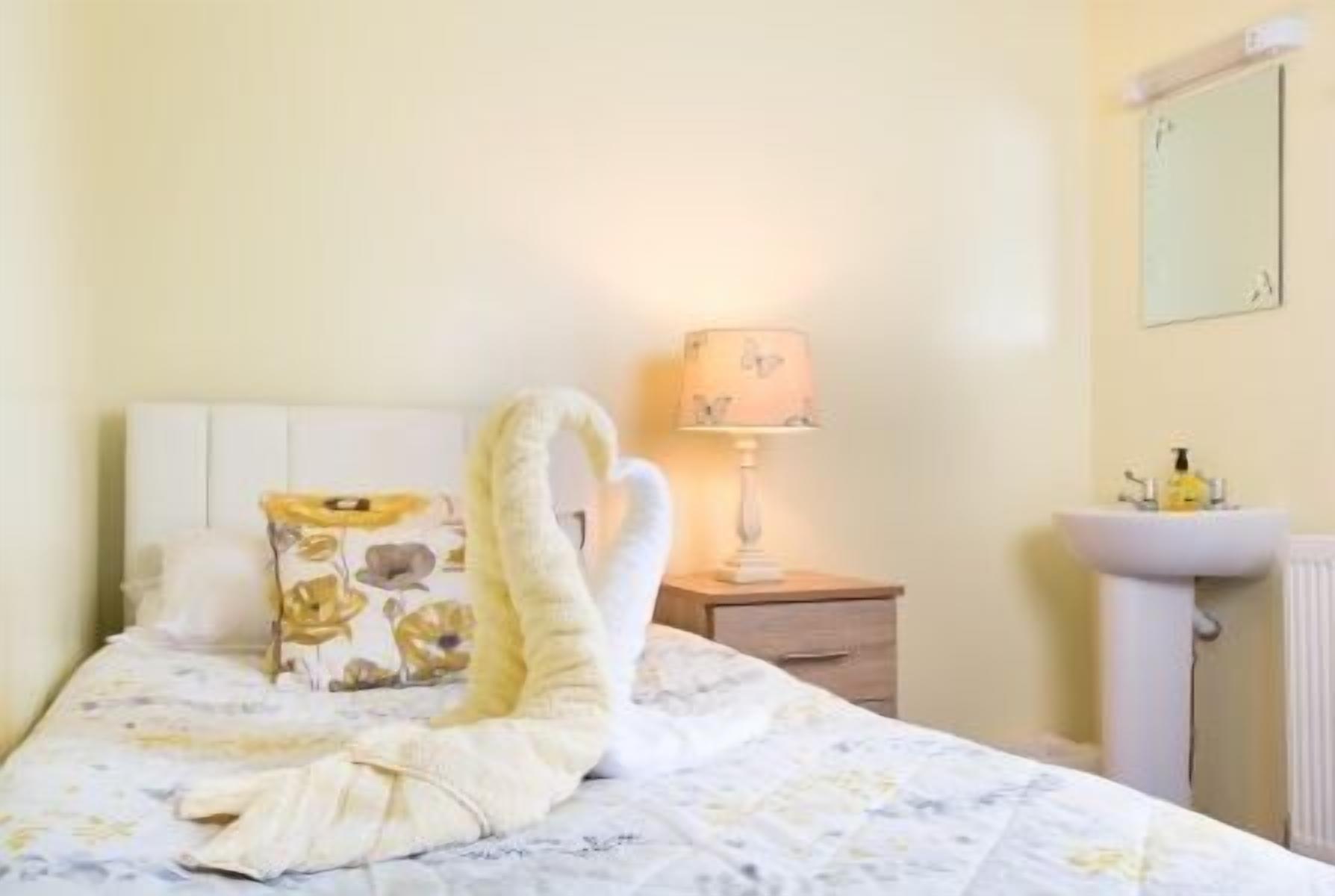 A hotel room with a bed, a bedside lamp, a nightstand, and a sink.