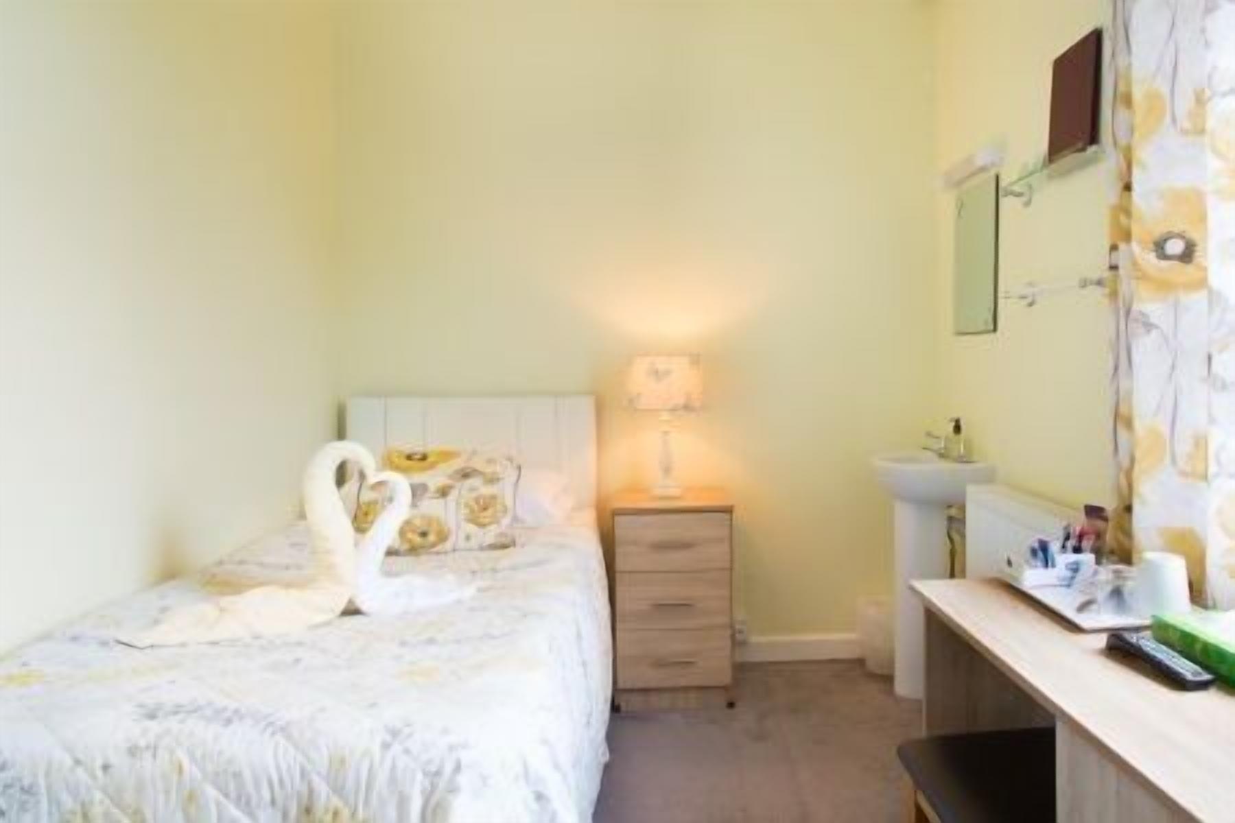 Une chambre à coucher avec un lit, une lampe de chevet, une commode, un miroir et un lavabo.