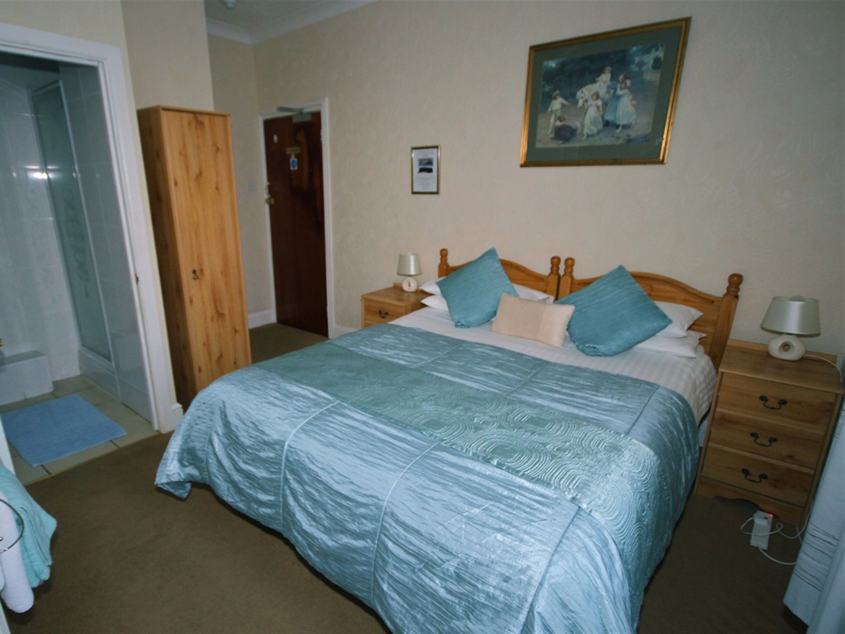 A bedroom with a large bed, wooden headboard, two bedside tables with lamps, a door, and a framed picture on the wall.