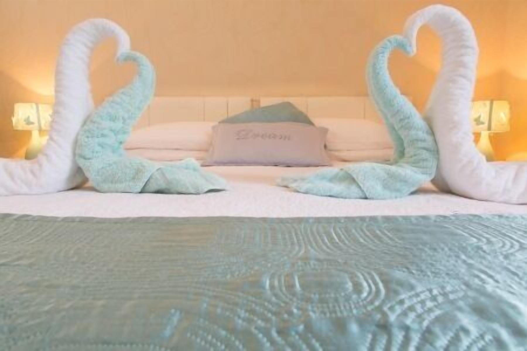 A bed with a white headboard, a pillow with the word "Dream" on it, and two swan-shaped towels.