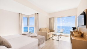 A hotel room with a bed, a sofa, a desk, a TV, and a balcony with a view of the sea. - CM Playa del Moro Hotel (Sant Llorenc des Cardassar)