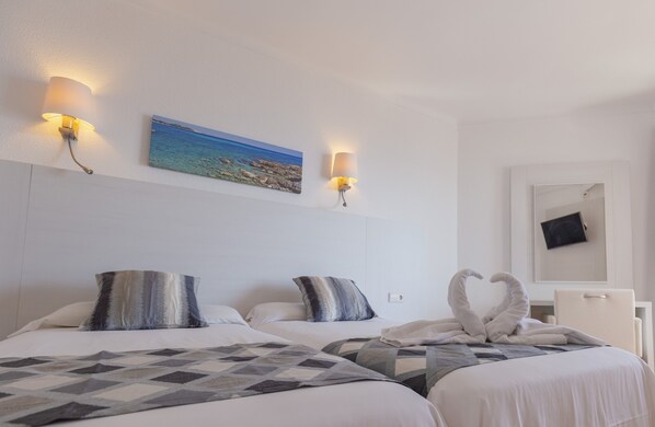 Une chambre d’hôtel avec deux lits, un tableau représentant une plage, des lampes fixées au mur et un miroir sur lequel est posé un objet noir.