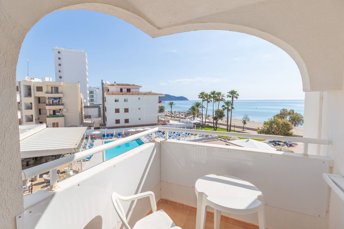 A balcony with a pool view, white furniture, and a clear view of the beach and ocean.
